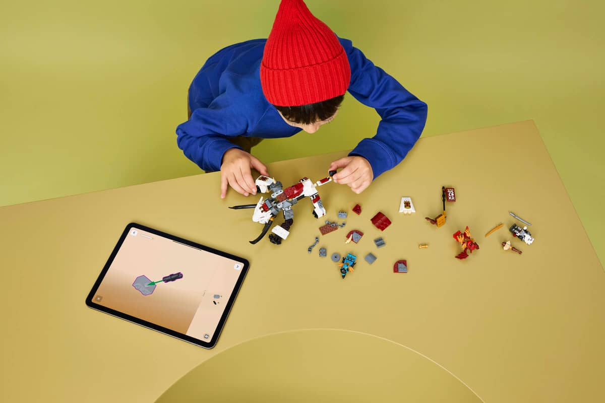 Criança a montar blocos de construção coloridos numa mesa com tablet ao lado