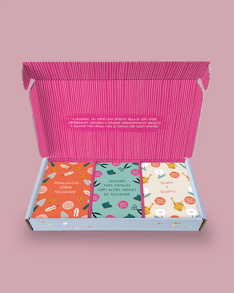 Caixa aberta com três baralhos de cartas coloridas para jogos familiares sobre felicidade.