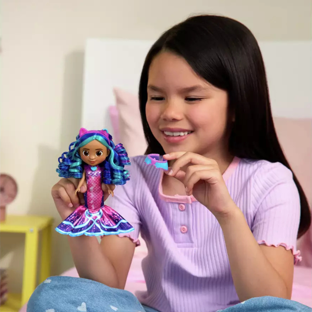 Menina a brincar com boneca azul e rosa sentada na cama