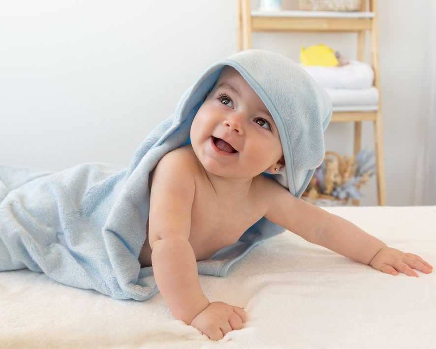 Bebé sorridente embrulhado numa toalha azul com capuz