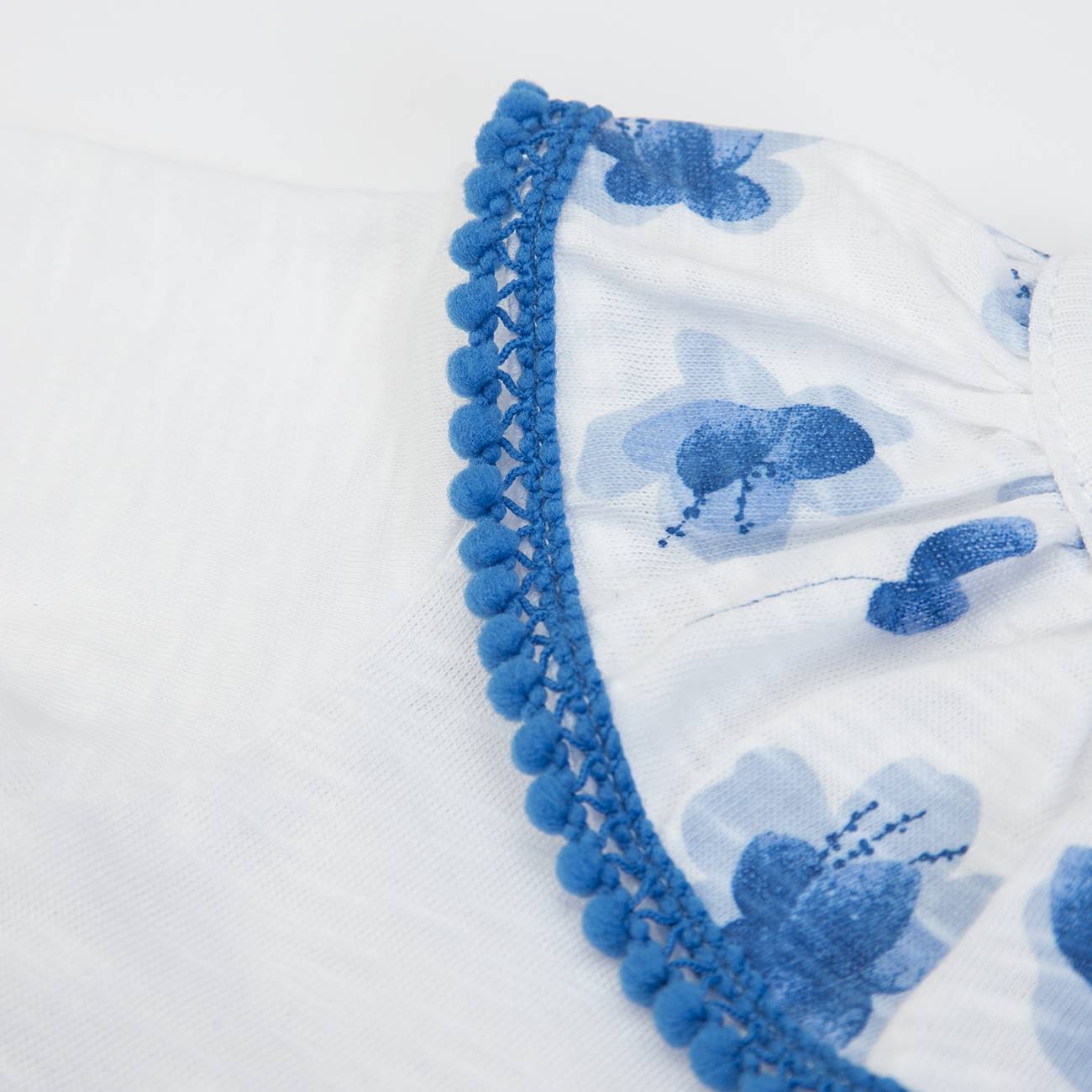 Peça de roupa branca com flores azuis e detalhe de pompom azul
