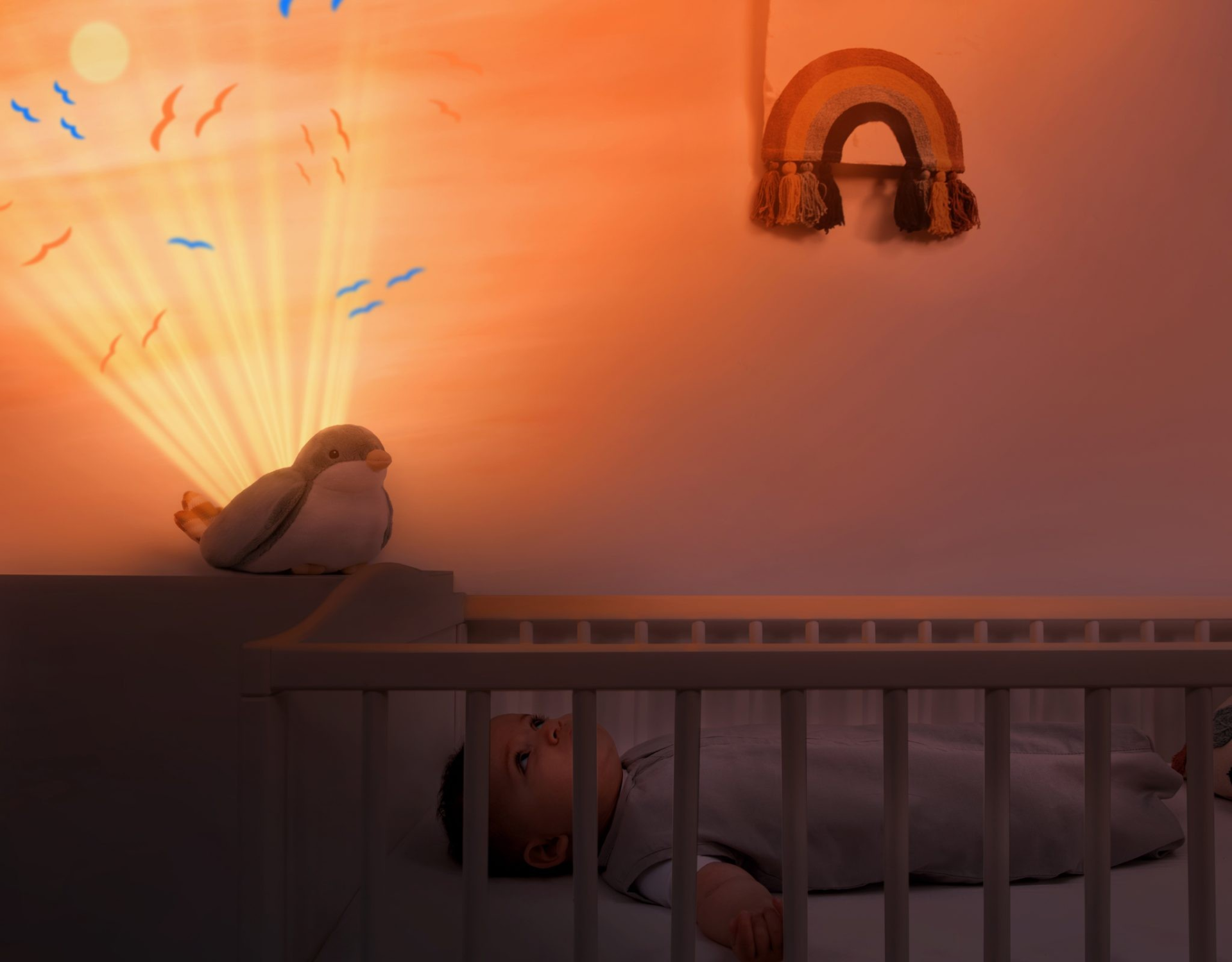 Abajur em forma de pássaro iluminando parede com silhuetas, bebé deitado em berço branco, decoração de parede colorida