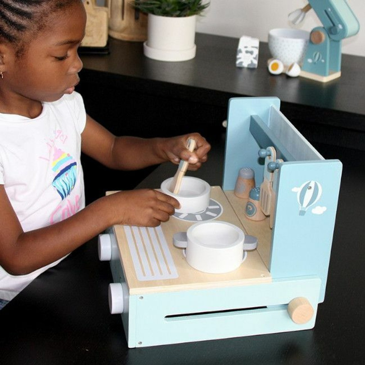 Criança a brincar com cozinha de brinquedo azul clara e madeira natural com acessórios