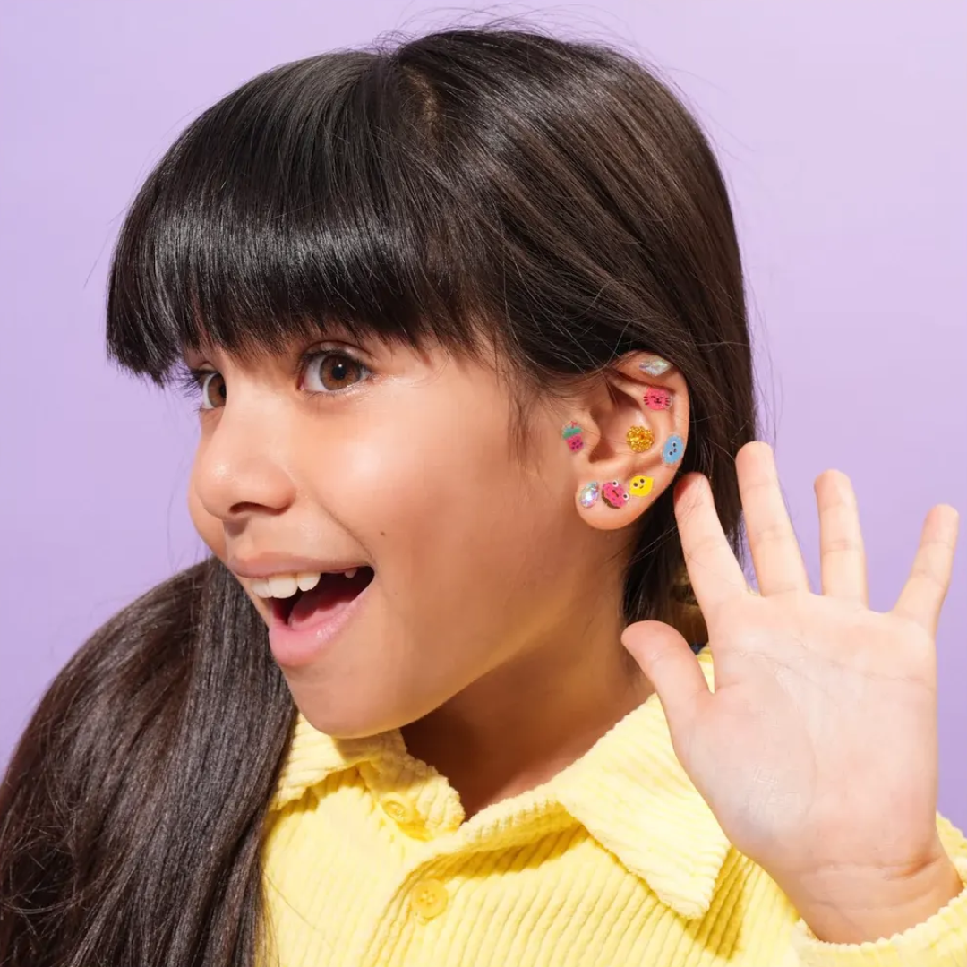 Menina com franja, camisa amarela e vários autocolantes coloridos na orelha direita.