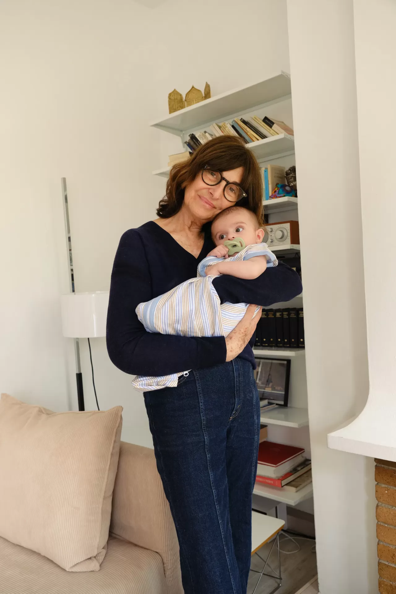 Mulher segurando bebé em casa com estantes ao fundo