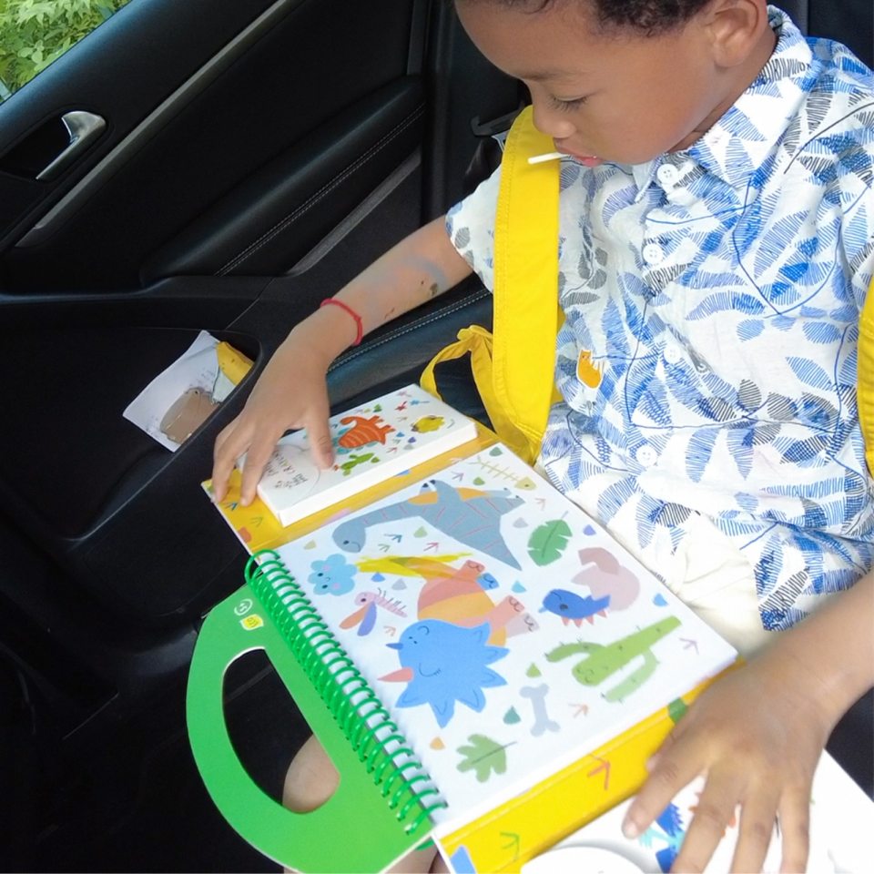 Livro interativo de dinossauros com capa amarela e alça verde aberto nas mãos de uma criança