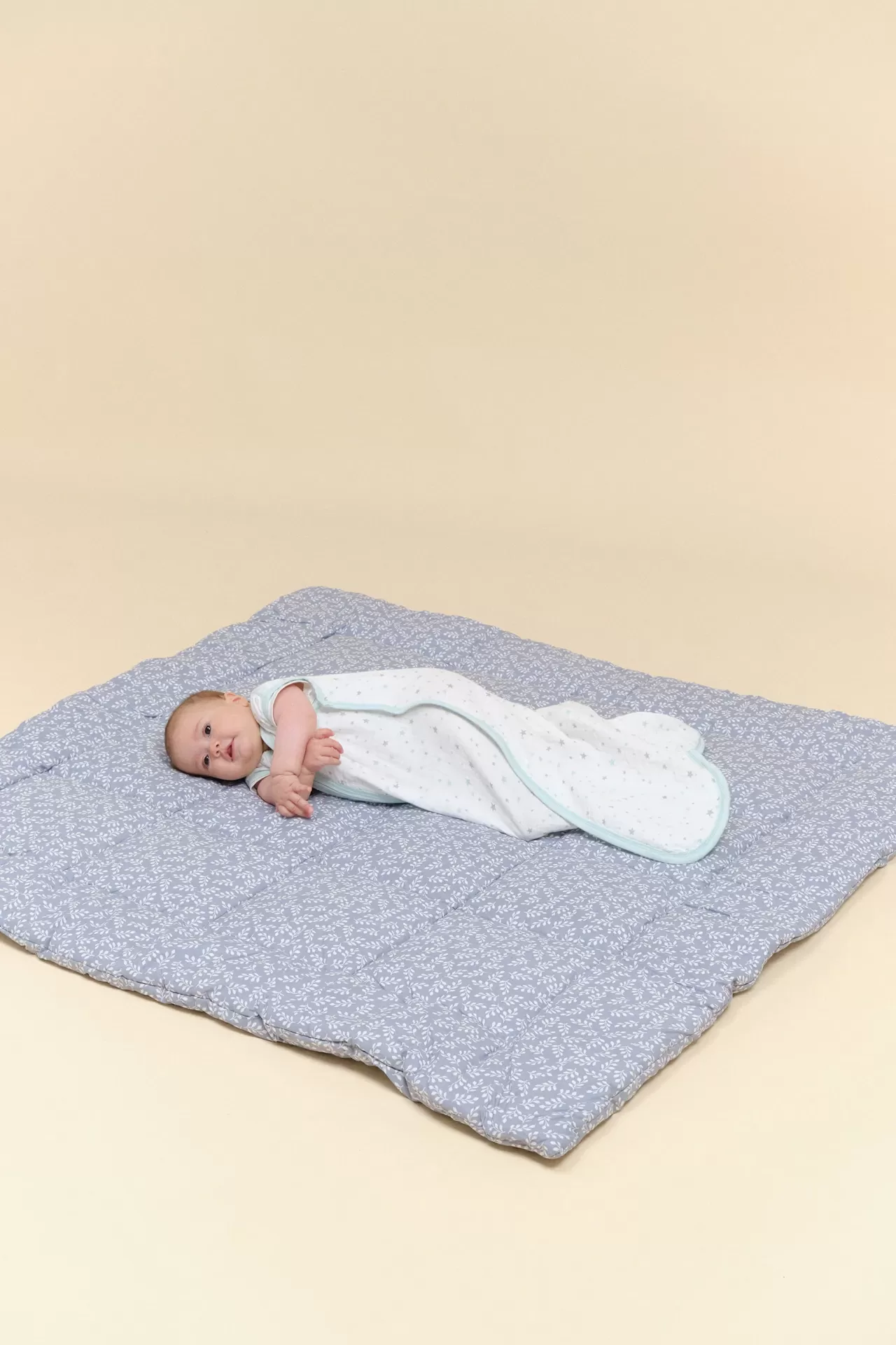 Bebé deitado numa almofada azul com padrões brancos sobre fundo bege