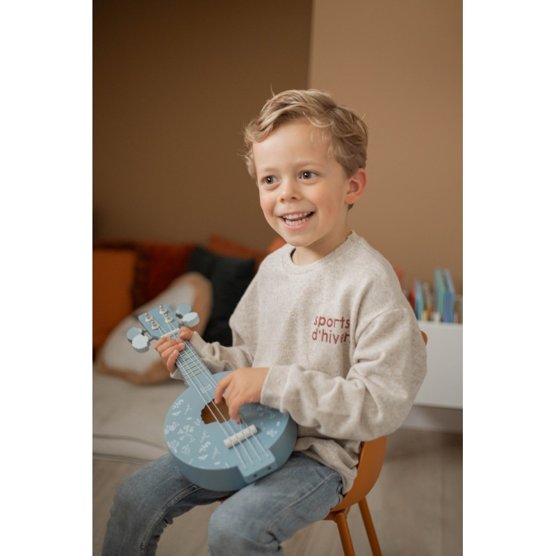 Criança com camisola cinzenta e calças de ganga a tocar ukulele azul claro com desenhos.
