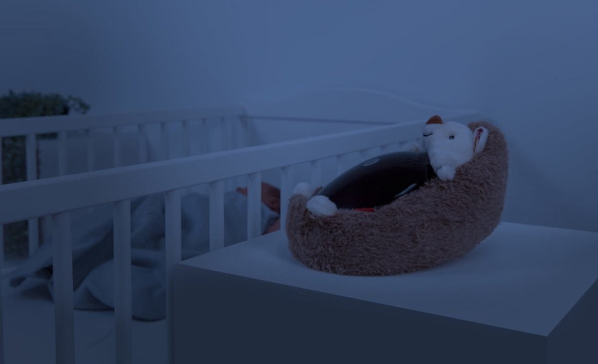 Berço branco com peluche castanha e branca em cima de mesa branca.