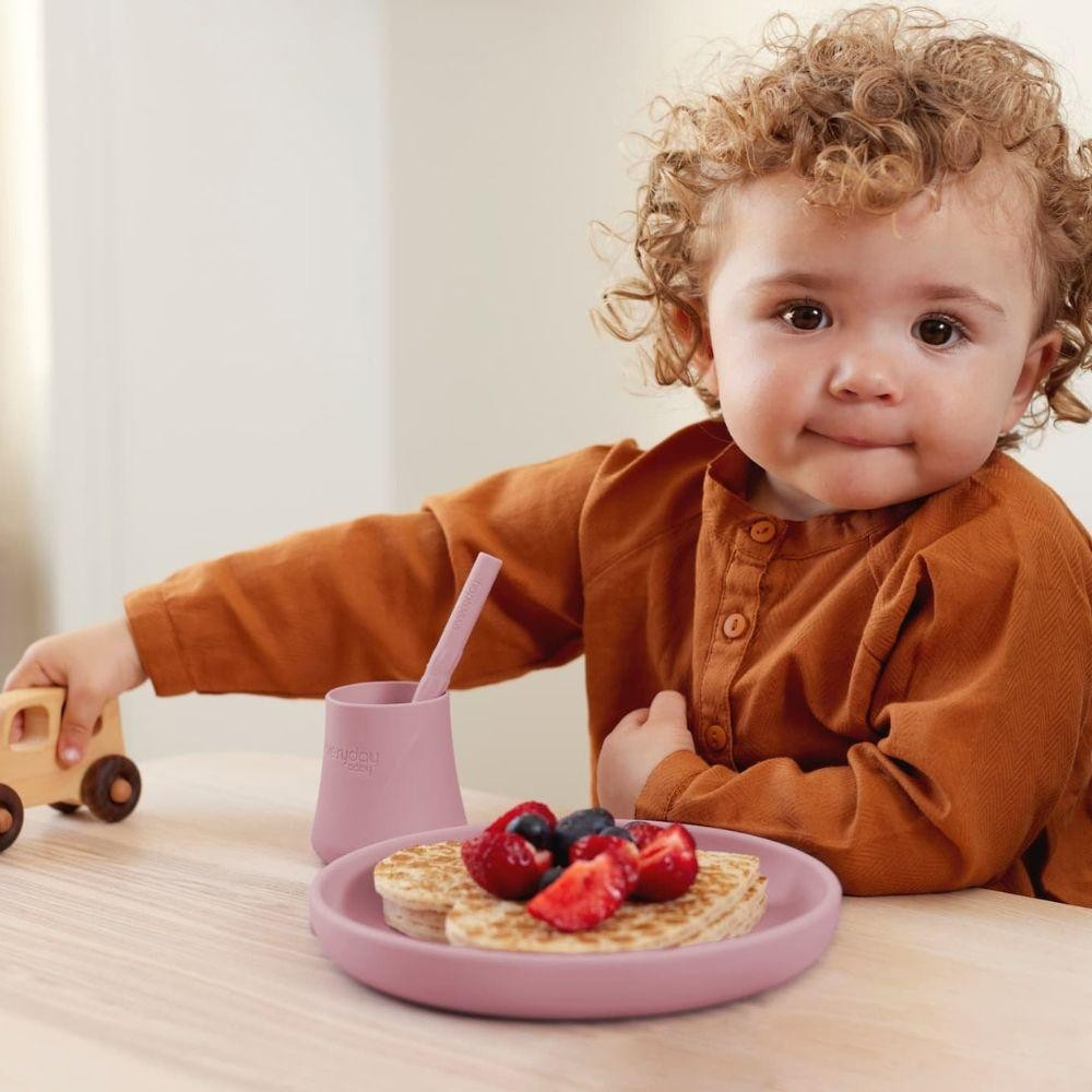 Criança com produto de refeição rosa e brinquedo de madeira numa mesa clara