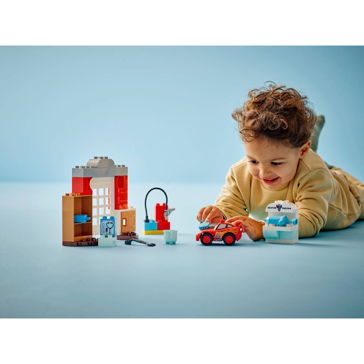 Criança a brincar com brinquedos de blocos de construção e um carro pequeno vermelho em fundo azul