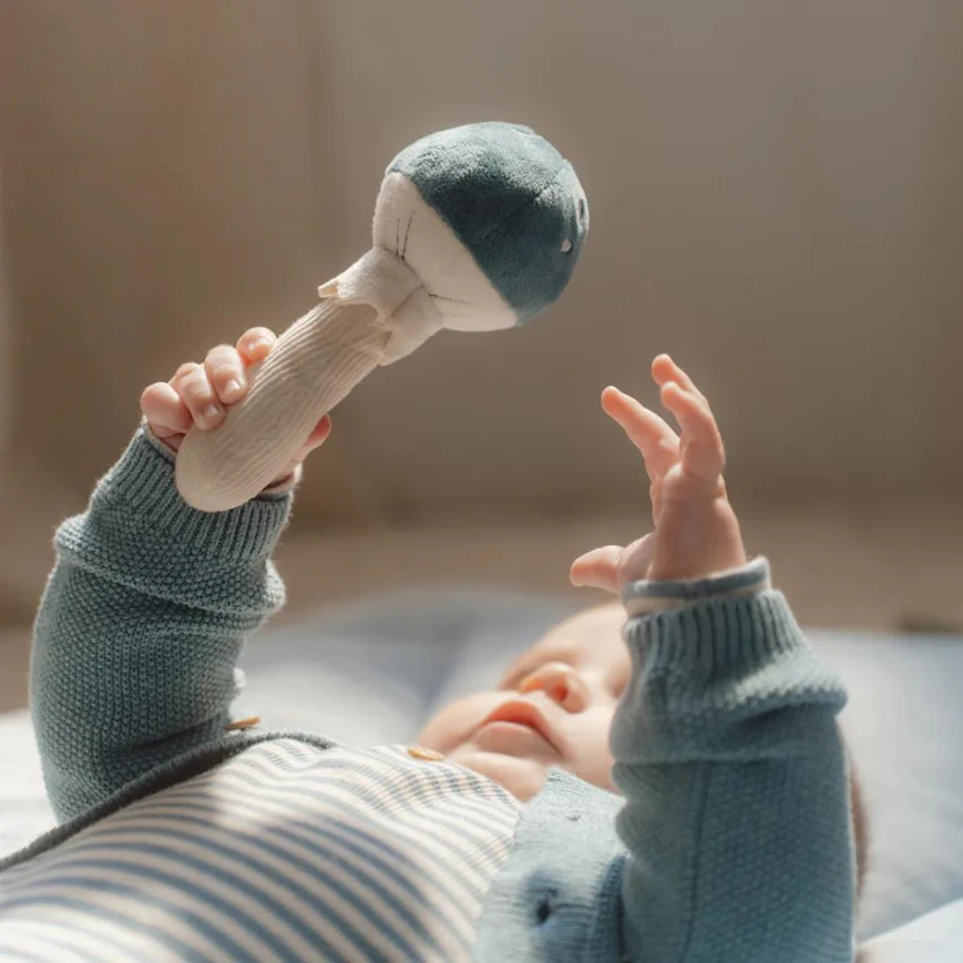 Boneco agarrável cinza e creme segurado por bebé de camisola cinza