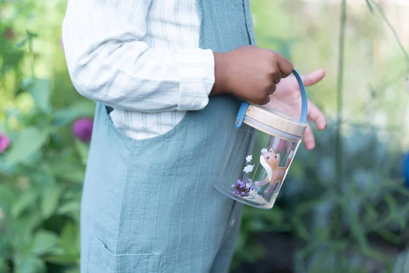 Criança segurando recipiente transparente decorado com raposa e flores.