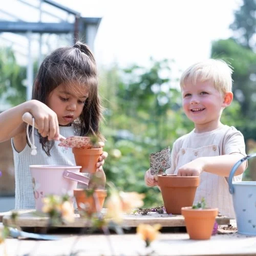 Crianças plantando em vasos de barro com baldes coloridos ao ar livre