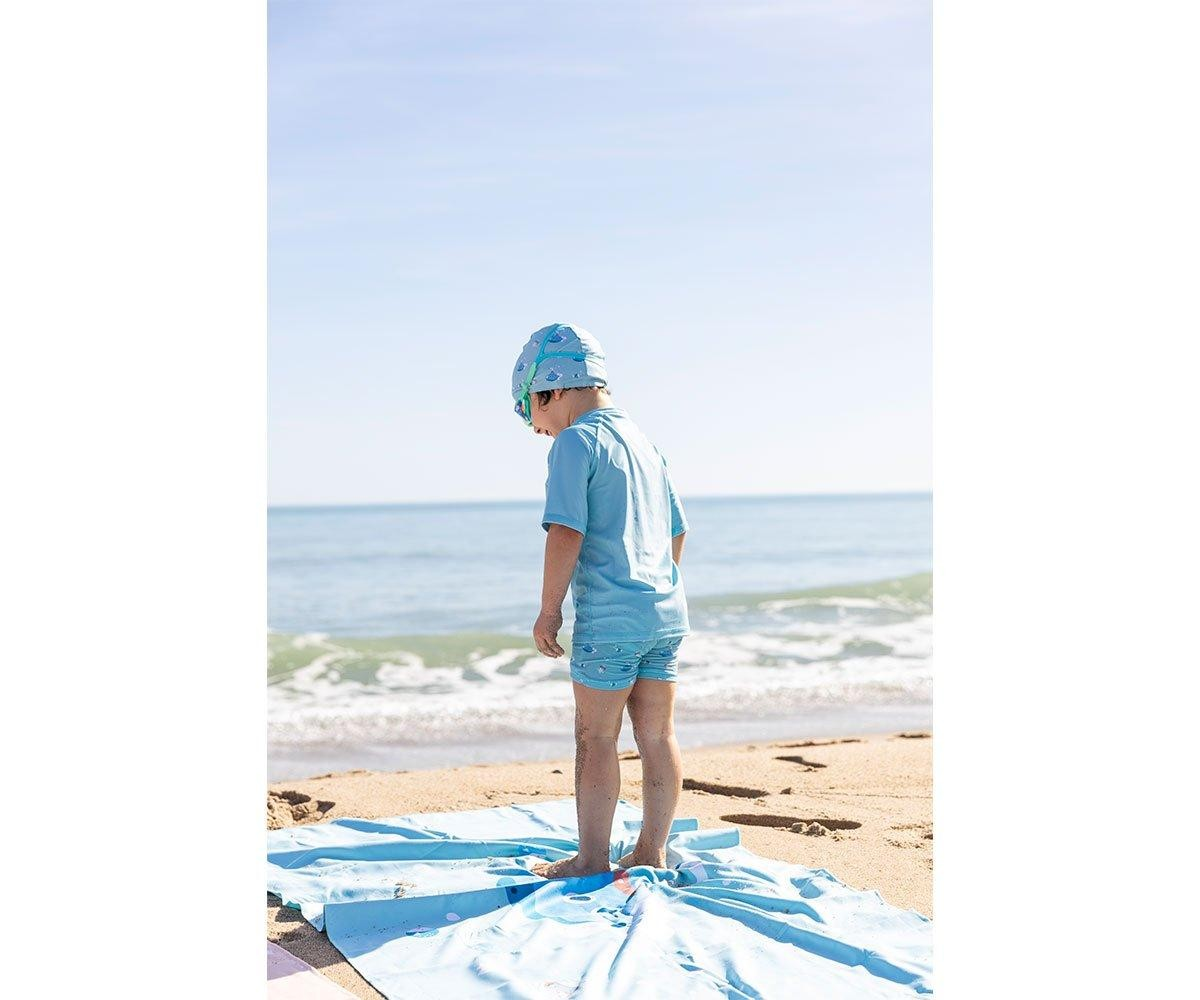 Criança de costas com roupa azul clara e chapéu na praia perto do mar