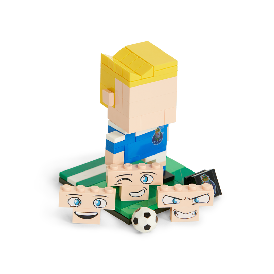 Figura Lego com cabelo amarelo, camiseta azul, três rostos intercambiáveis e bola de futebol.