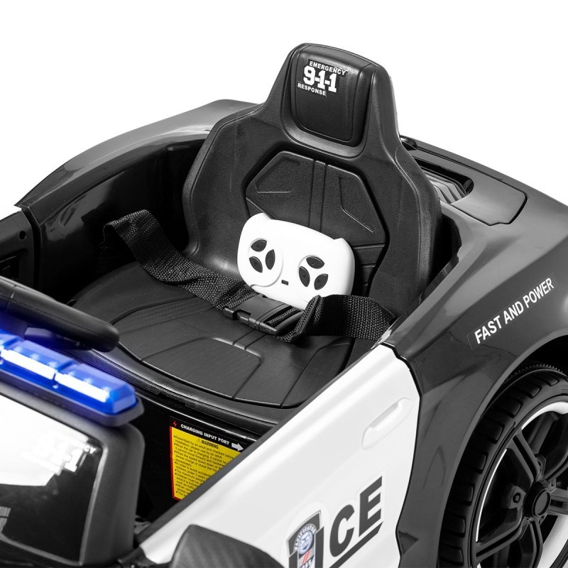 Cadeira preta com cinto de segurança e controle remoto dentro de carro de polícia infantil preto e branco.