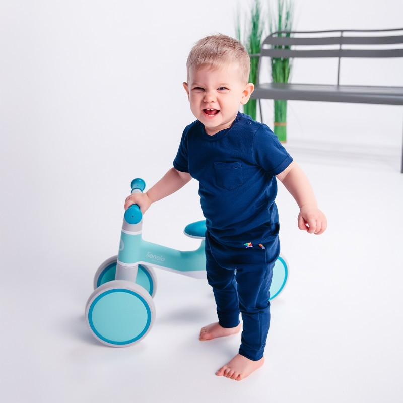 Criança com roupa azul e trotador azul claro em ambiente branco com banco e plantas