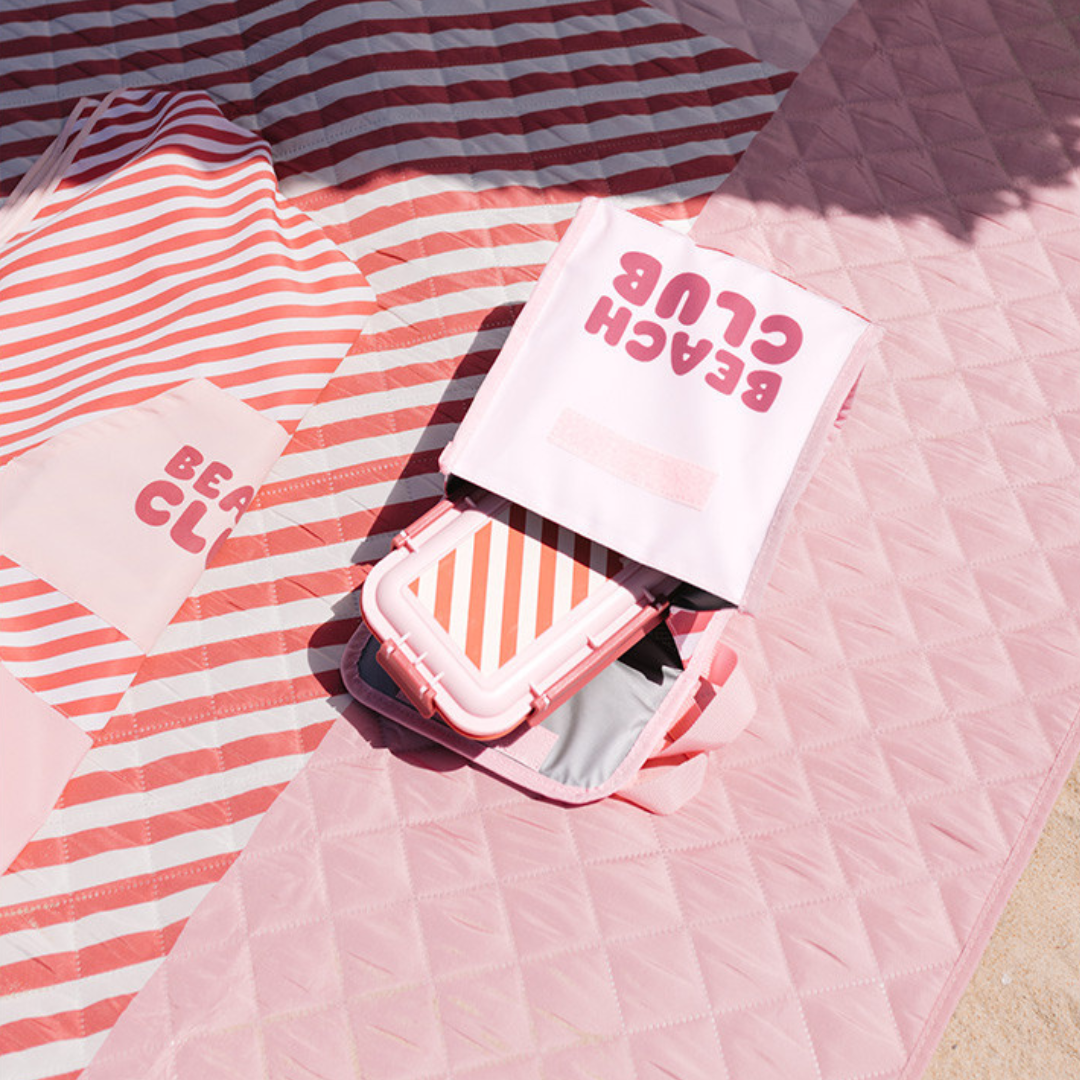 Tapetes de praia rosa e branco com bolsa rosa claro e caixa listrada na areia