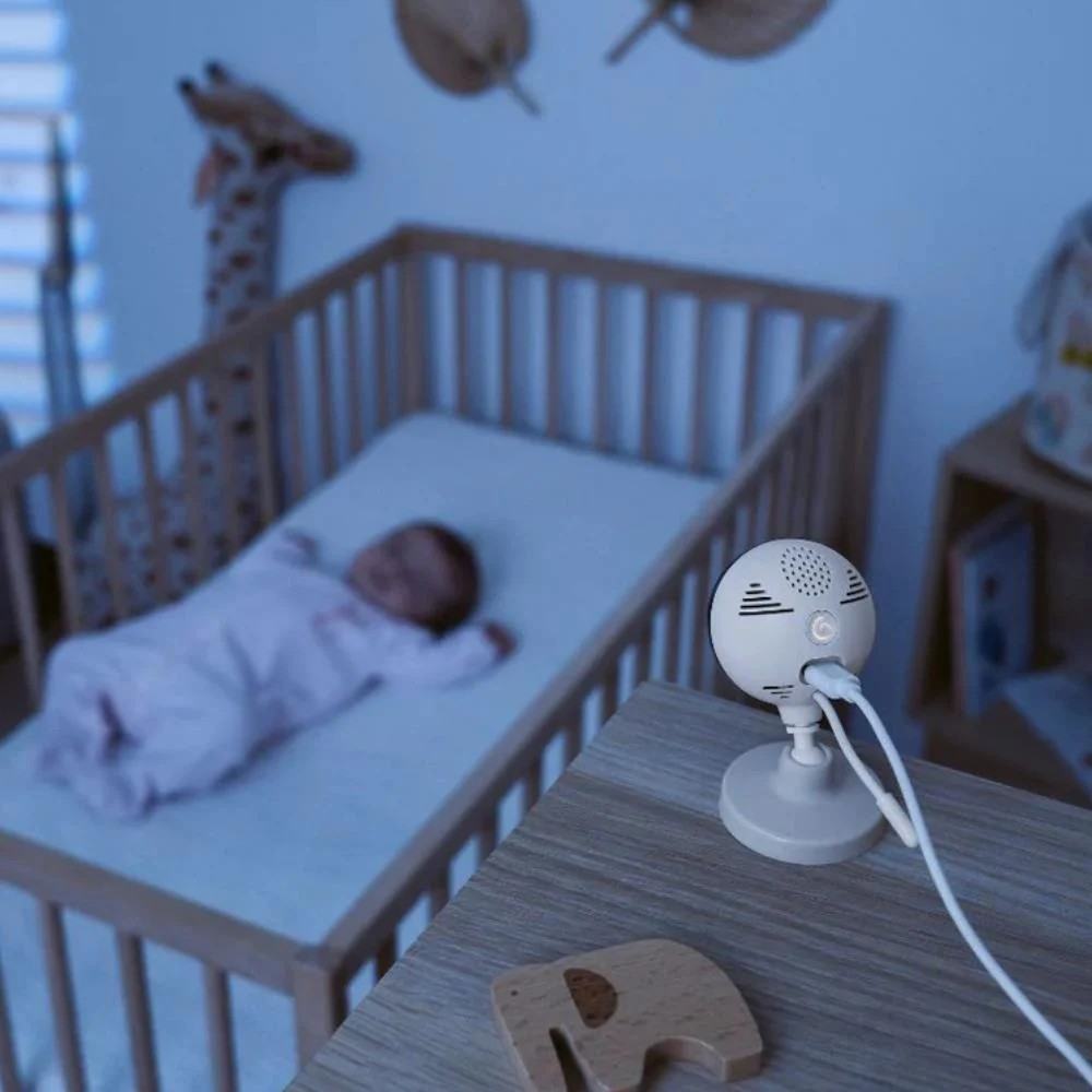 Monitor branco para bebé, berço de madeira com bebé a dormir e brinquedo girafa ao fundo