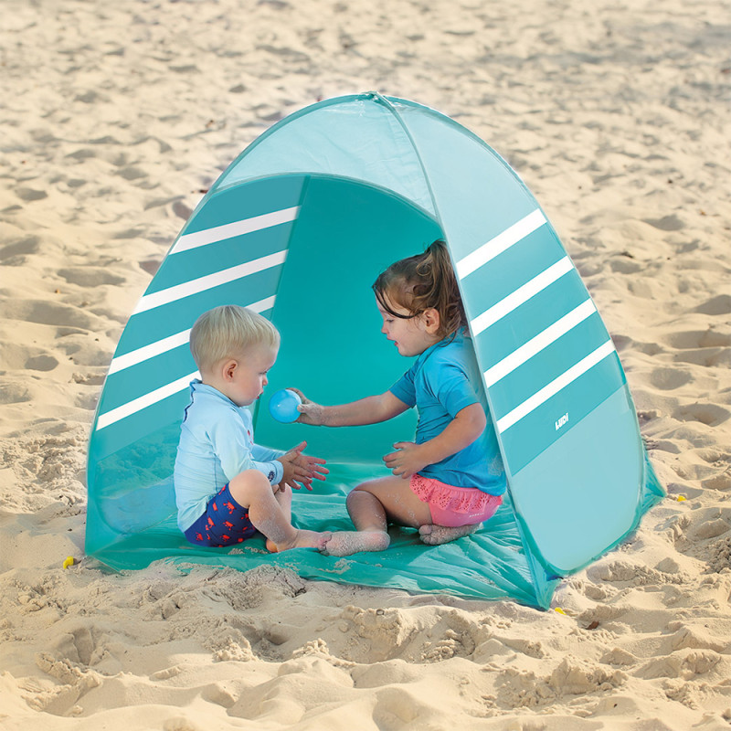 Tenda de praia azul com riscas brancas na areia com duas crianças a brincar no interior