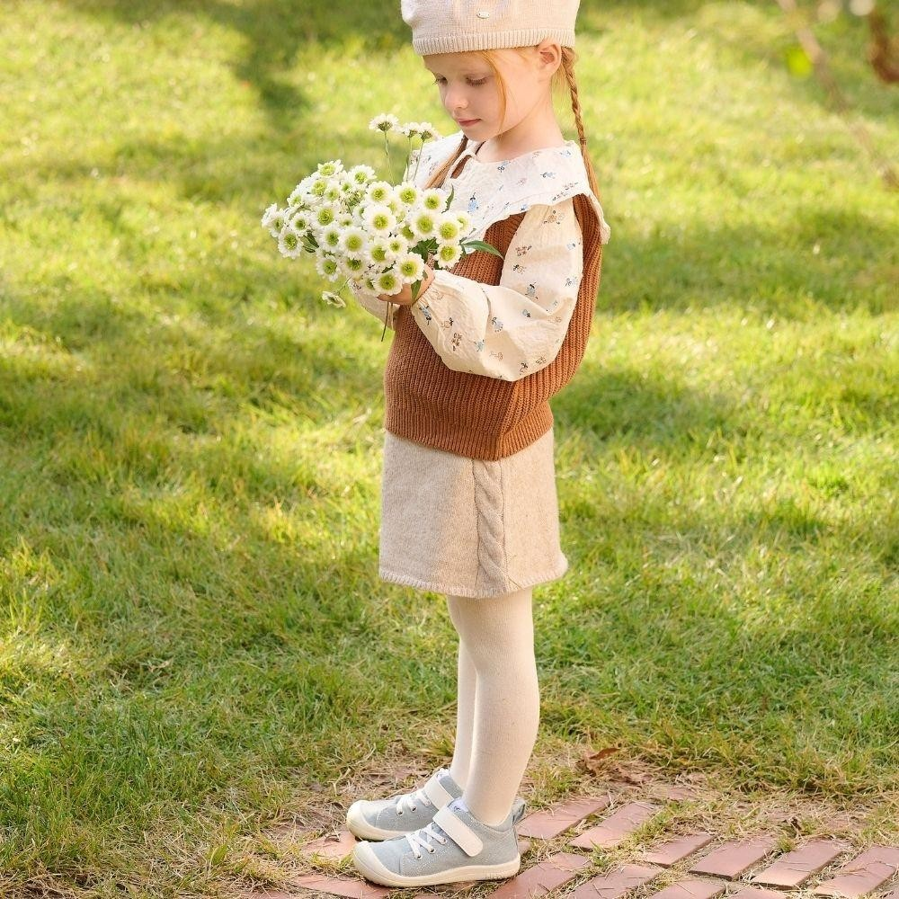 Menina com roupa castanha e bege segurando margaridas no jardim