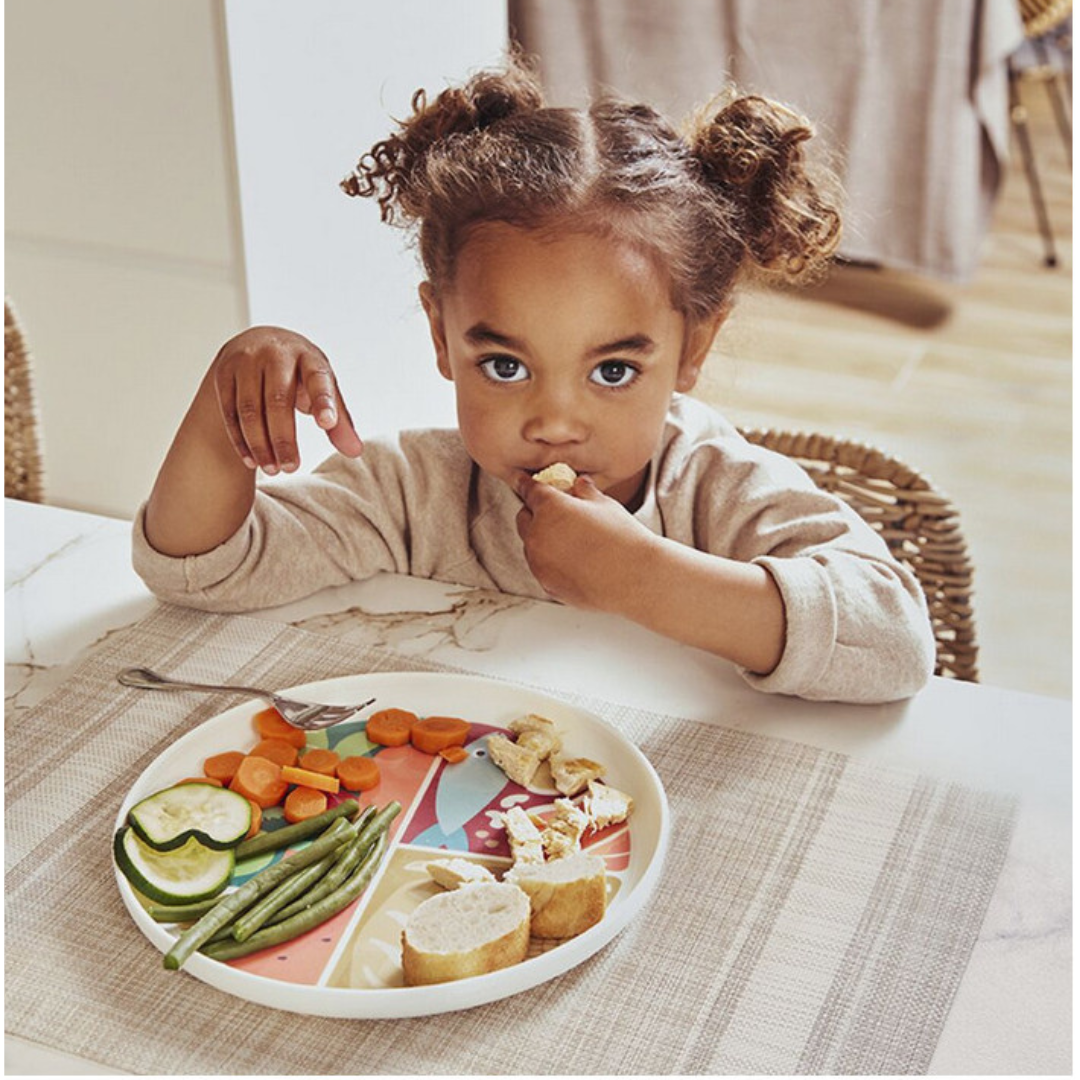 Prato colorido dividido em quatro seções com comida e criança a comer