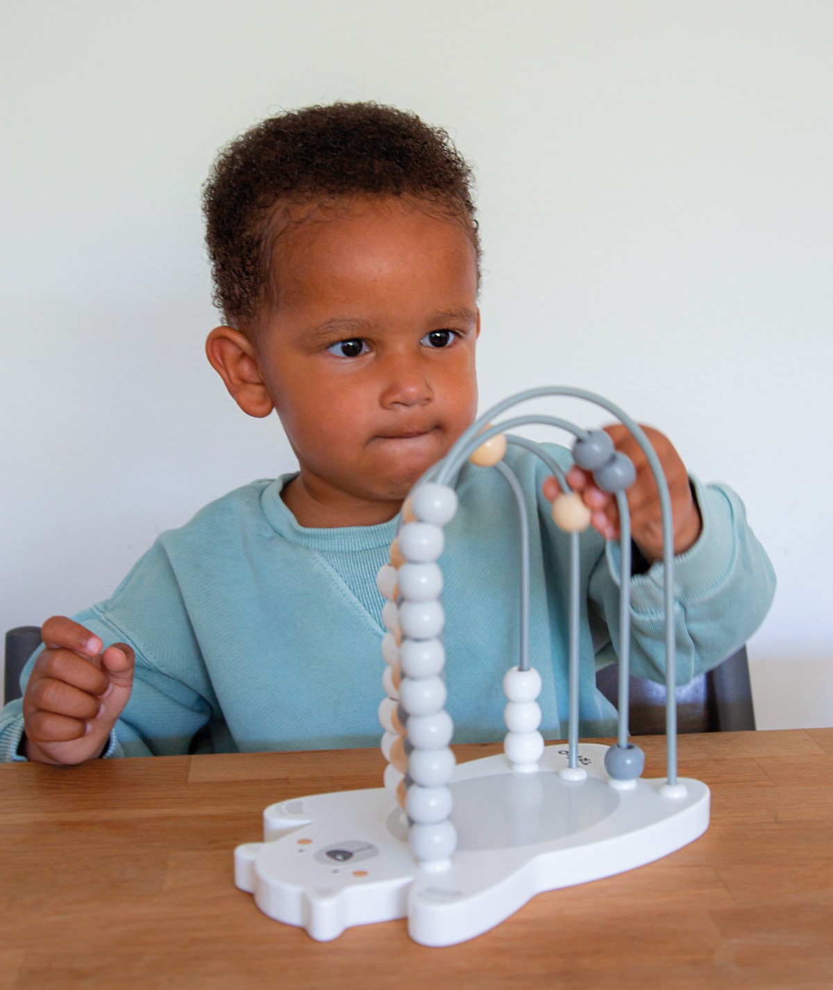 Criança a brincar com brinquedo educativo de contas coloridas em arcos de metal cinzento