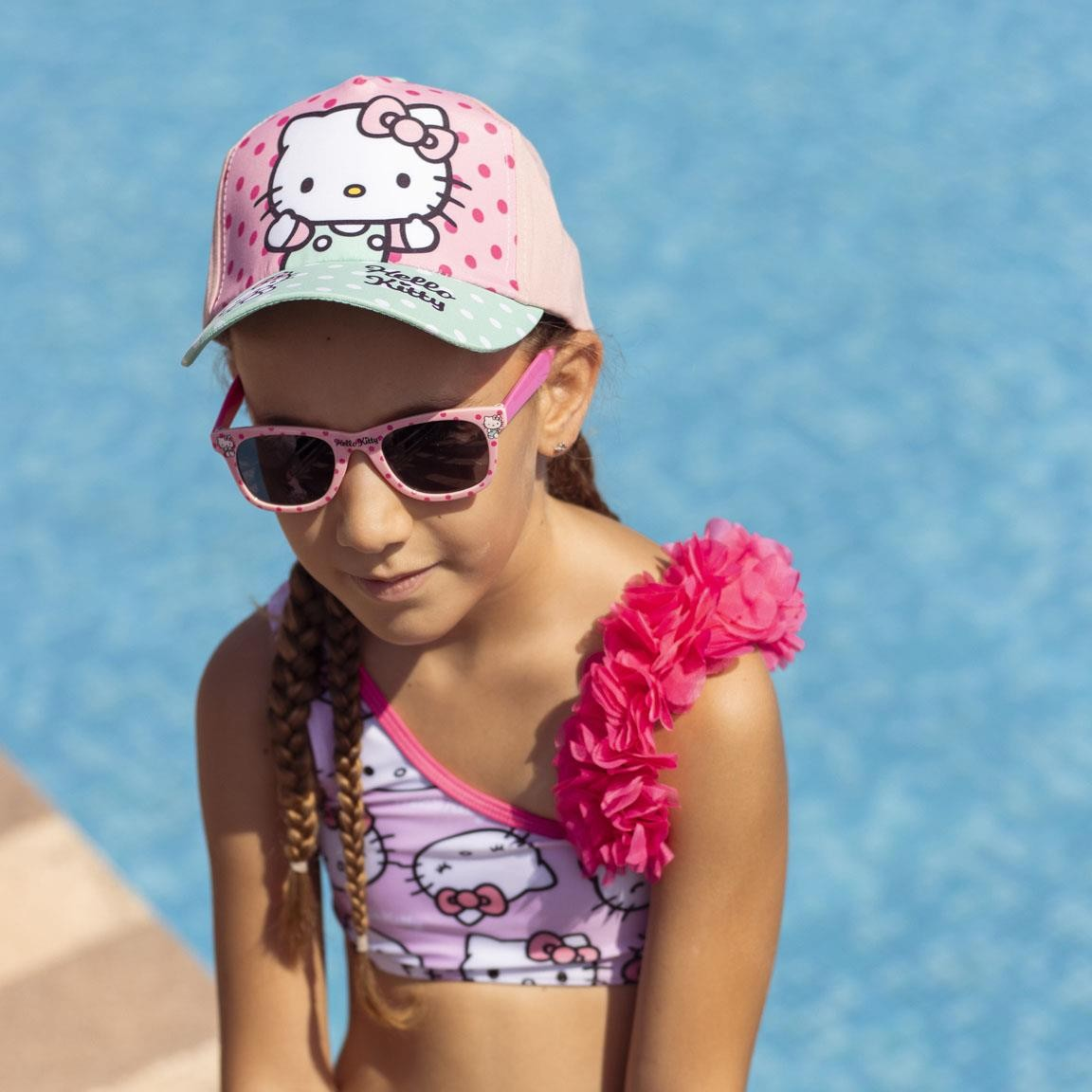 Menina com fato de banho Hello Kitty e boné rosa junto a piscina