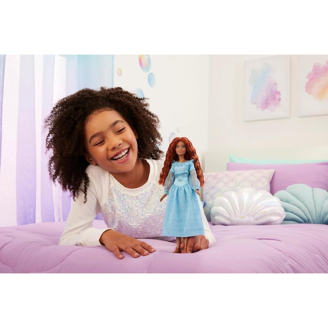 Boneca vestida de azul numa cama lilás com uma criança sorridente ao lado