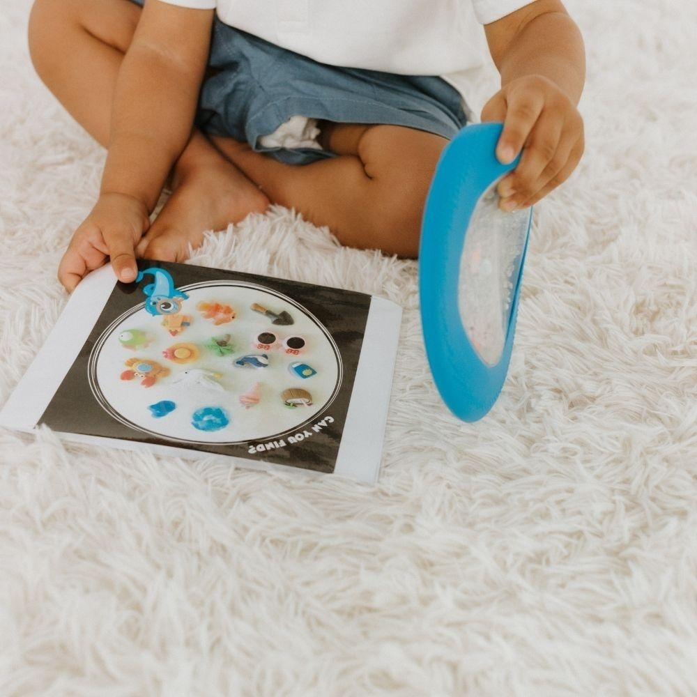 Criança com brinquedo educativo azul e placa colorida em superfície branca macia