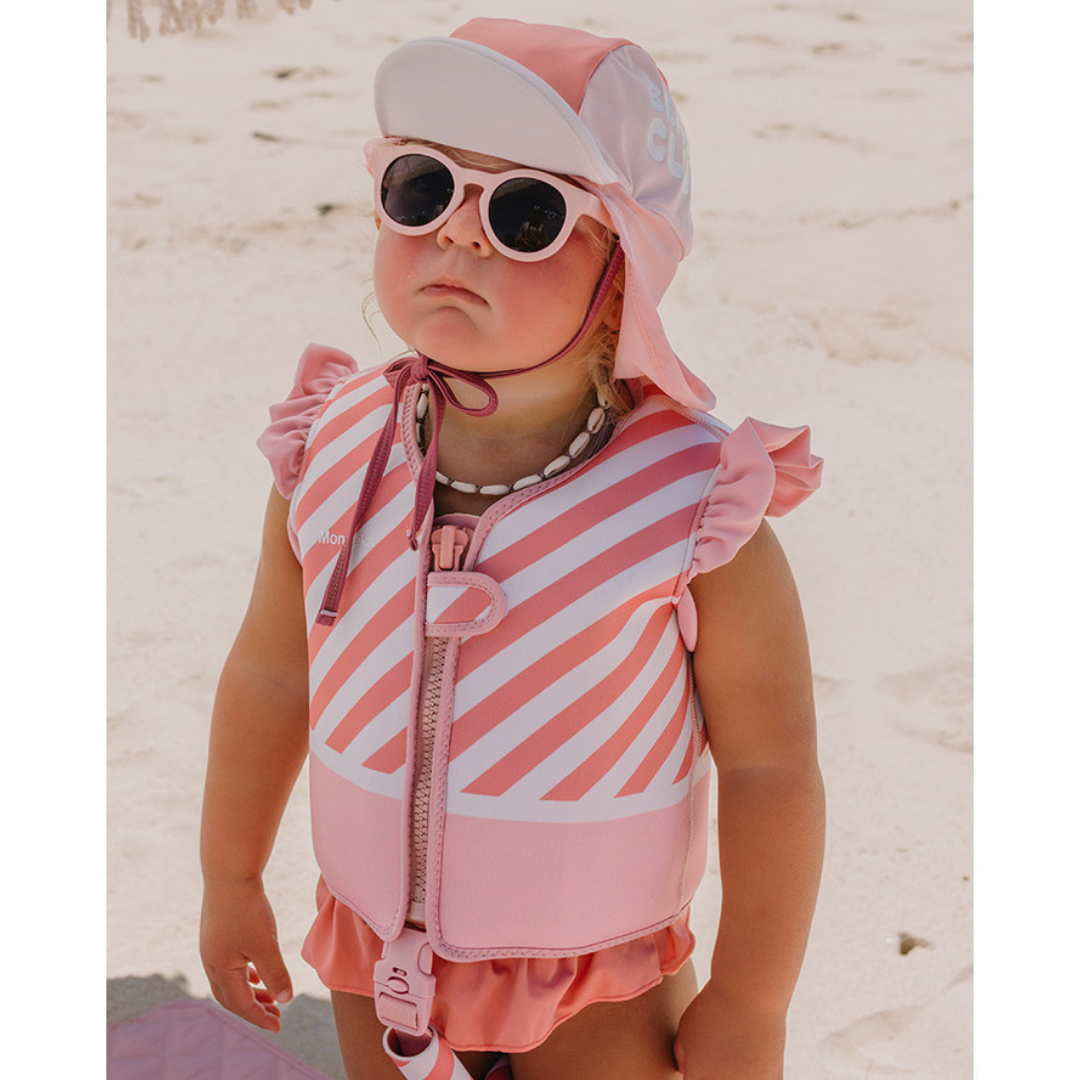 Criança com colete salva-vidas rosa e chapéu de sol numa praia