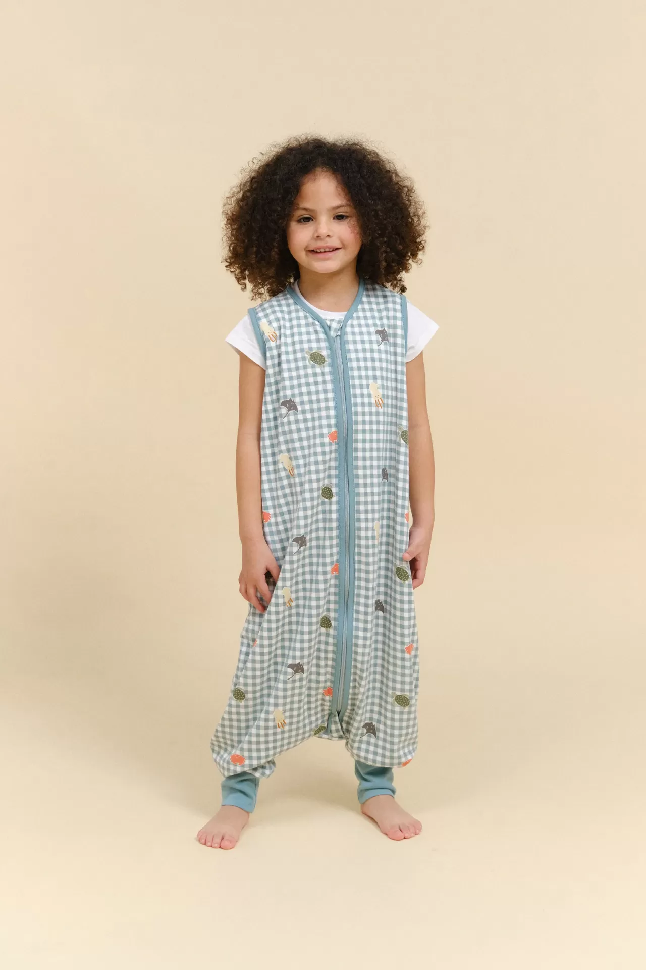 Criança com macacão de dormir azul claro com padrão de quadrados e desenhos coloridos