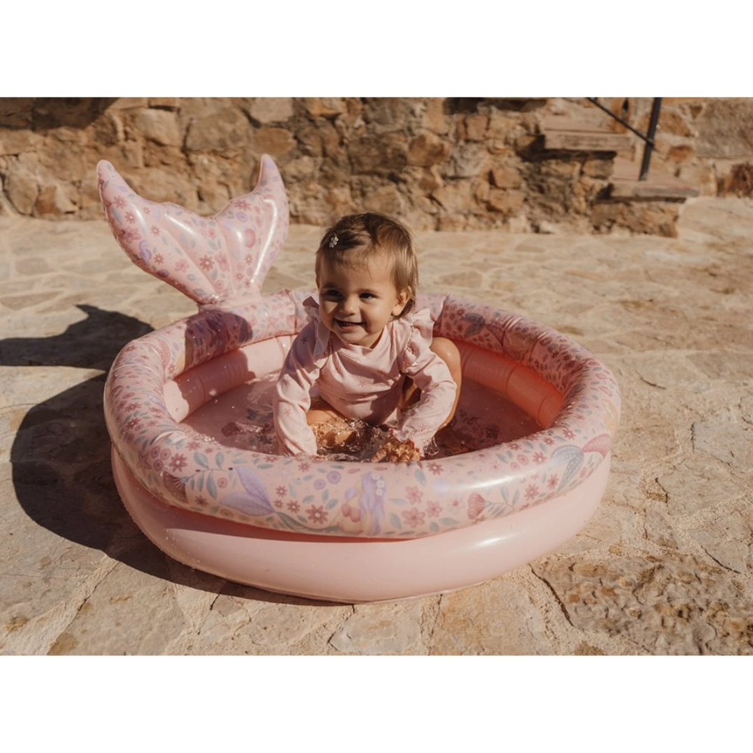 Piscina insuflável infantil rosa com padrão floral e cauda de sereia, criança a brincar com água