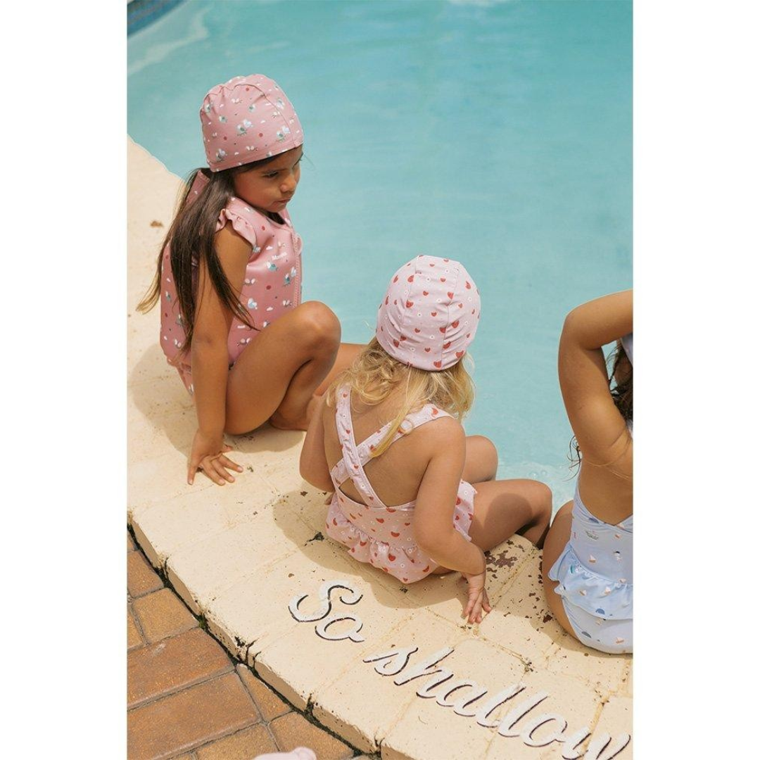 Crianças com fatos de banho e toucas sentadas na borda de uma piscina azul