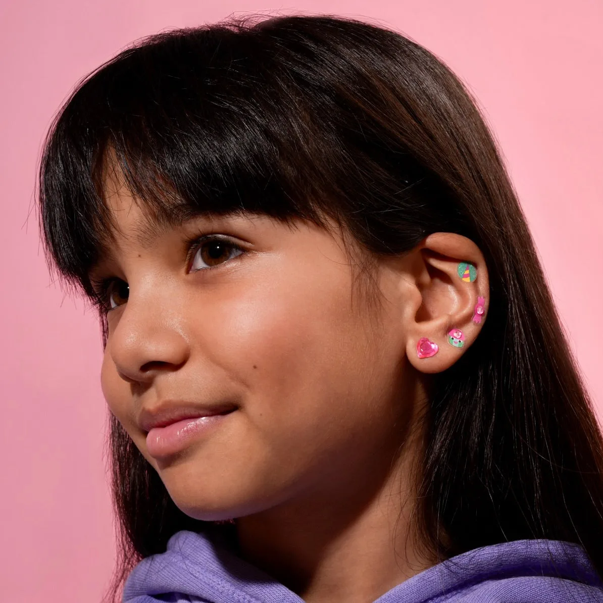 Brincos coloridos de plástico em menina com fundo rosa