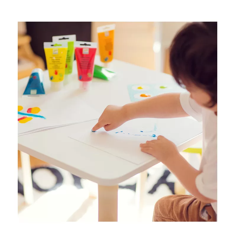 Criança a pintar numa mesa branca com tinta colorida em tubos.