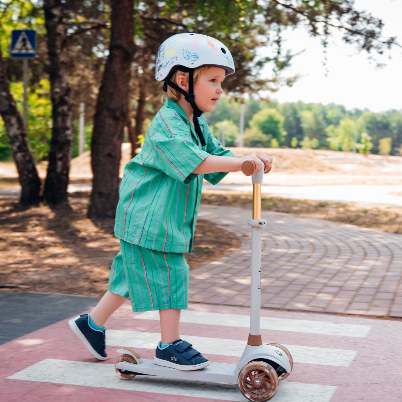 Criança em trotinete branca com capacete e fato verde às riscas numa passadeira outdoors