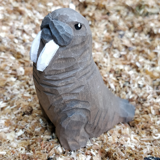 Figurino de morsa em madeira com presas brancas e olhos pretos sobre aparas de madeira