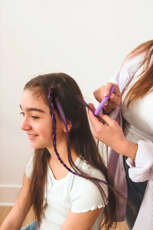 Cabelo castanho com mechas roxas sendo aplicado a uma rapariga com camisola branca