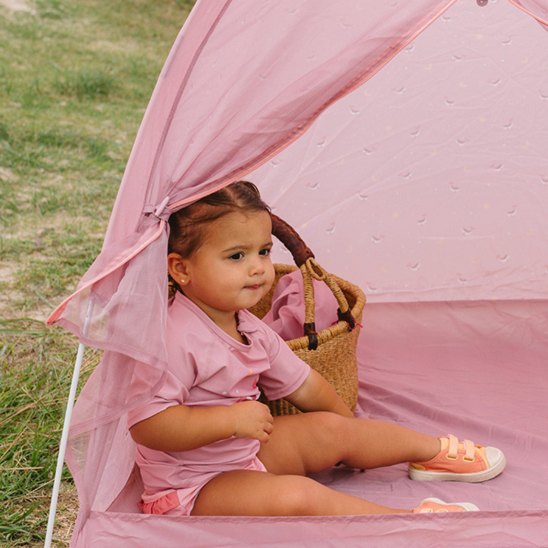 Menina sentada numa tenda rosa ao ar livre com uma cesta de palha