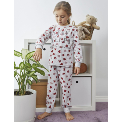 Pijama infantil cinzento claro com corações vermelhos e texto, criança descalça em quarto com tapete roxo e móveis brancos.