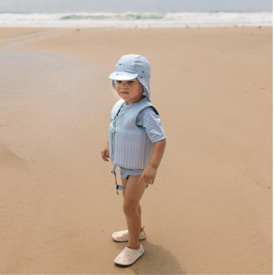 Criança com colete salva-vidas e chapéu azul numa praia de areia
