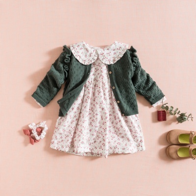 Conjunto infantil com vestido floral branco e rosa, casaco verde, sapatinhos camel, tudo sobre fundo rosa claro