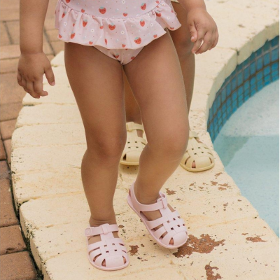 Criança com fato de banho de morangos e sandálias de plástico rosa junto à piscina