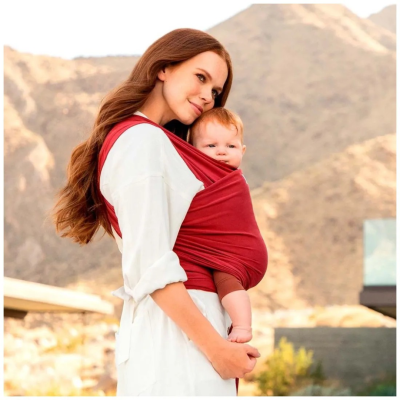 Mãe a transportar bebé num sling vermelho ao ar livre com montanhas ao fundo