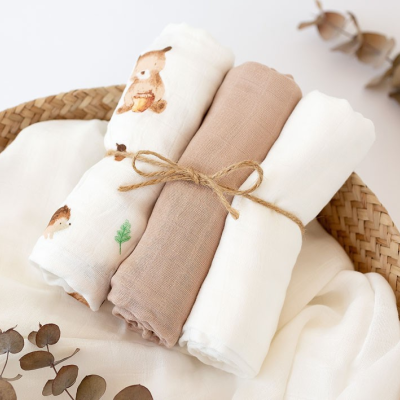 Conjunto de três panos enrolados e amarrados com corda, com padrão de ursos, liso castanho claro e branco, numa bandeja de aranha com folhas secas.