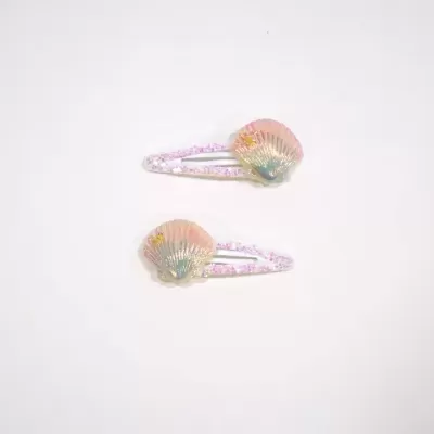 Dois ganchos de cabelo com conchas decorativas em fundo branco.