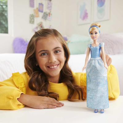 Boneca princesa com vestido azul e branco e criança sorridente ao fundo em ambiente interior