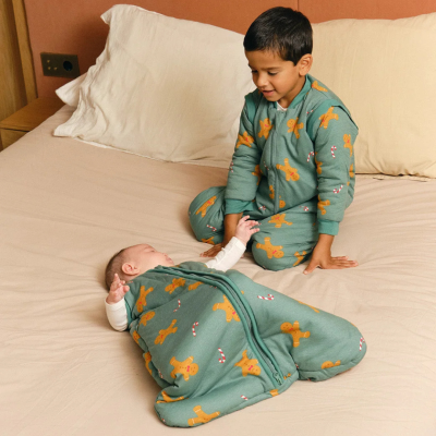 Criança e bebé com pijamas verdes com biscoitos de gengibre na cama beige.